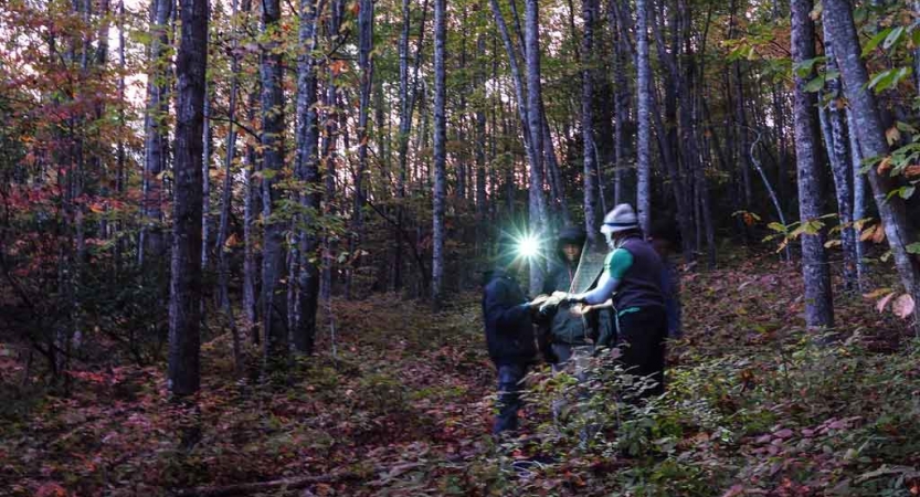 students wearing headlamps look at a map on a backpacking trip in north carolina